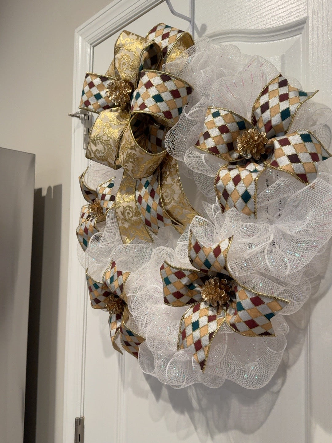 Side view of handmade white and gold Christmas wreath with layered ribbons and gold pinecones