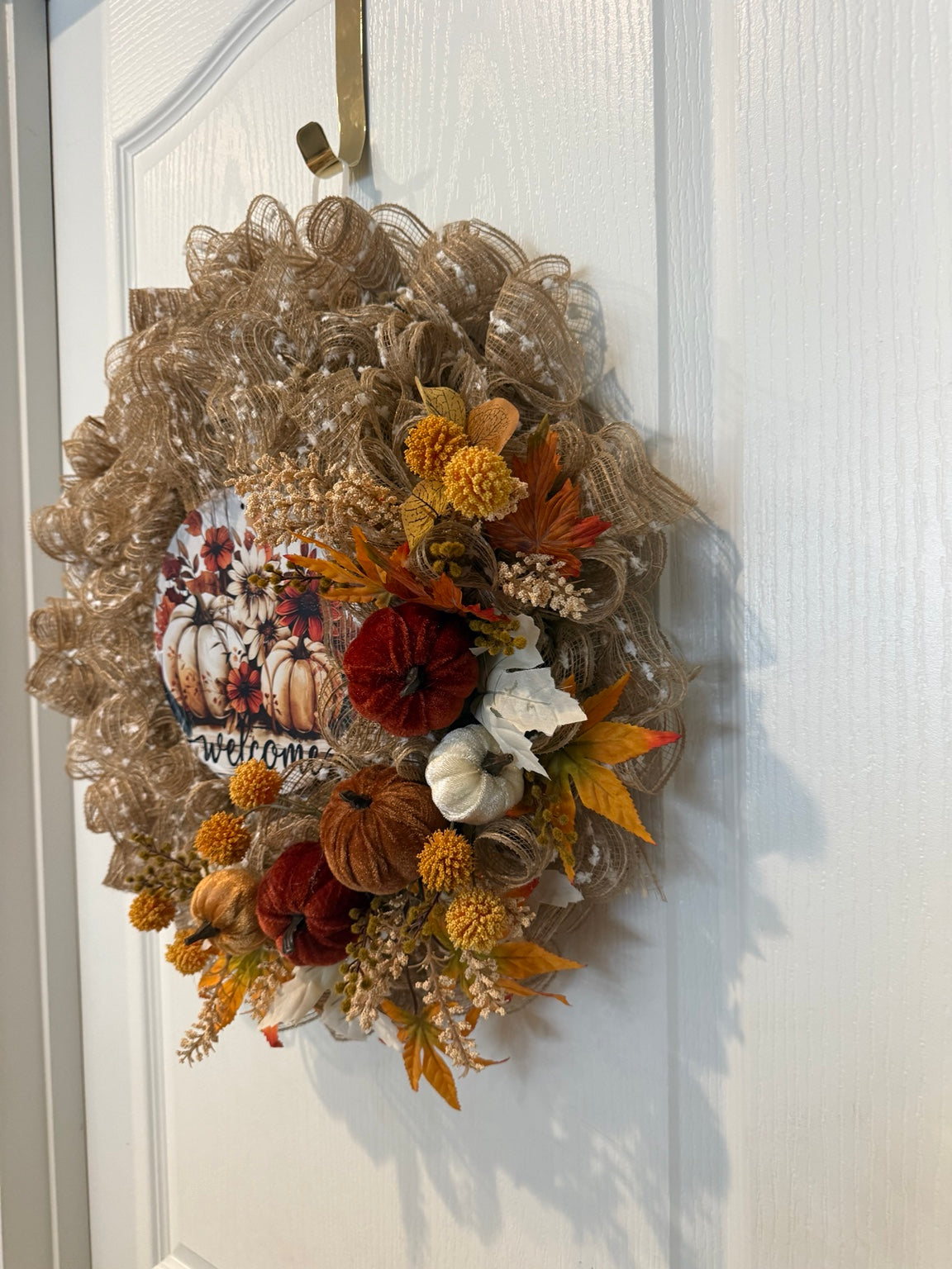 Close view of handmade fall pumpkin wreath with welcome sign and autumn florals
